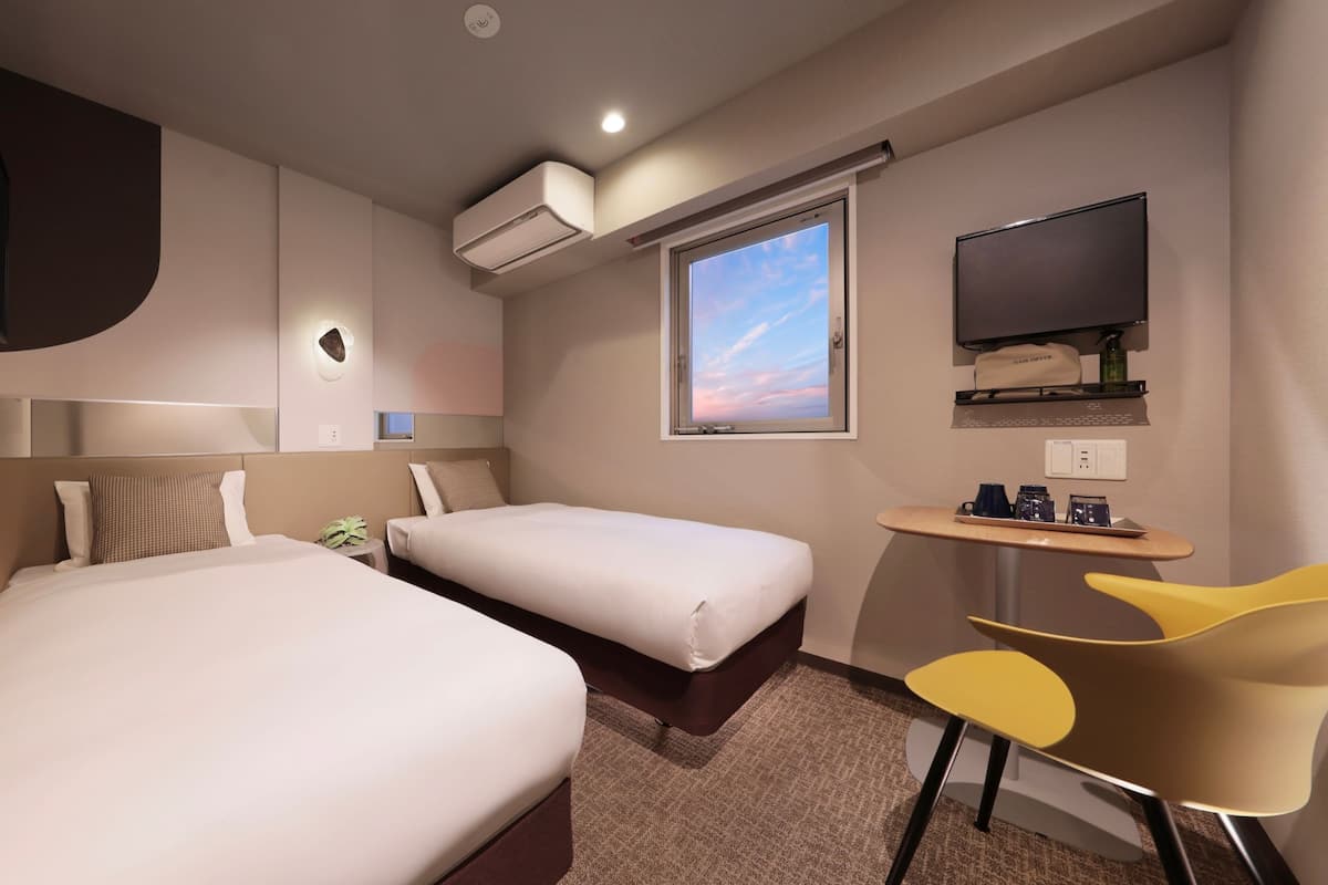 Une chambre d’hôtel avec deux lits, un bureau avec une chaise, une télévision et un appareil de climatisation.