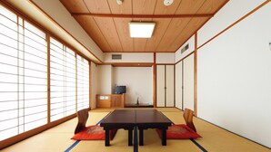 A tatami mat room with a low table and cushions, wooden sliding doors, and a television in the background. - Nagasaki IK Hotel (Nagasaki)