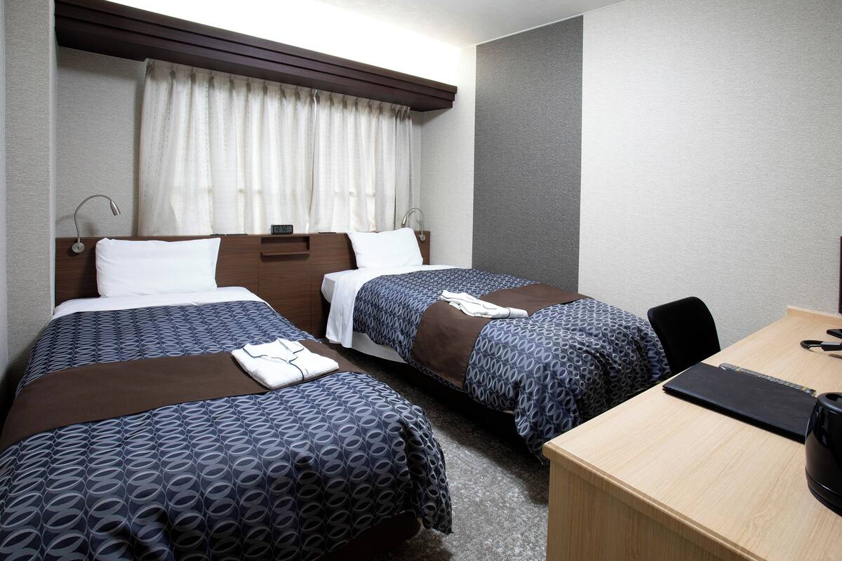 Een hotelkamer met twee bedden, een bureau en een raam met gordijnen.