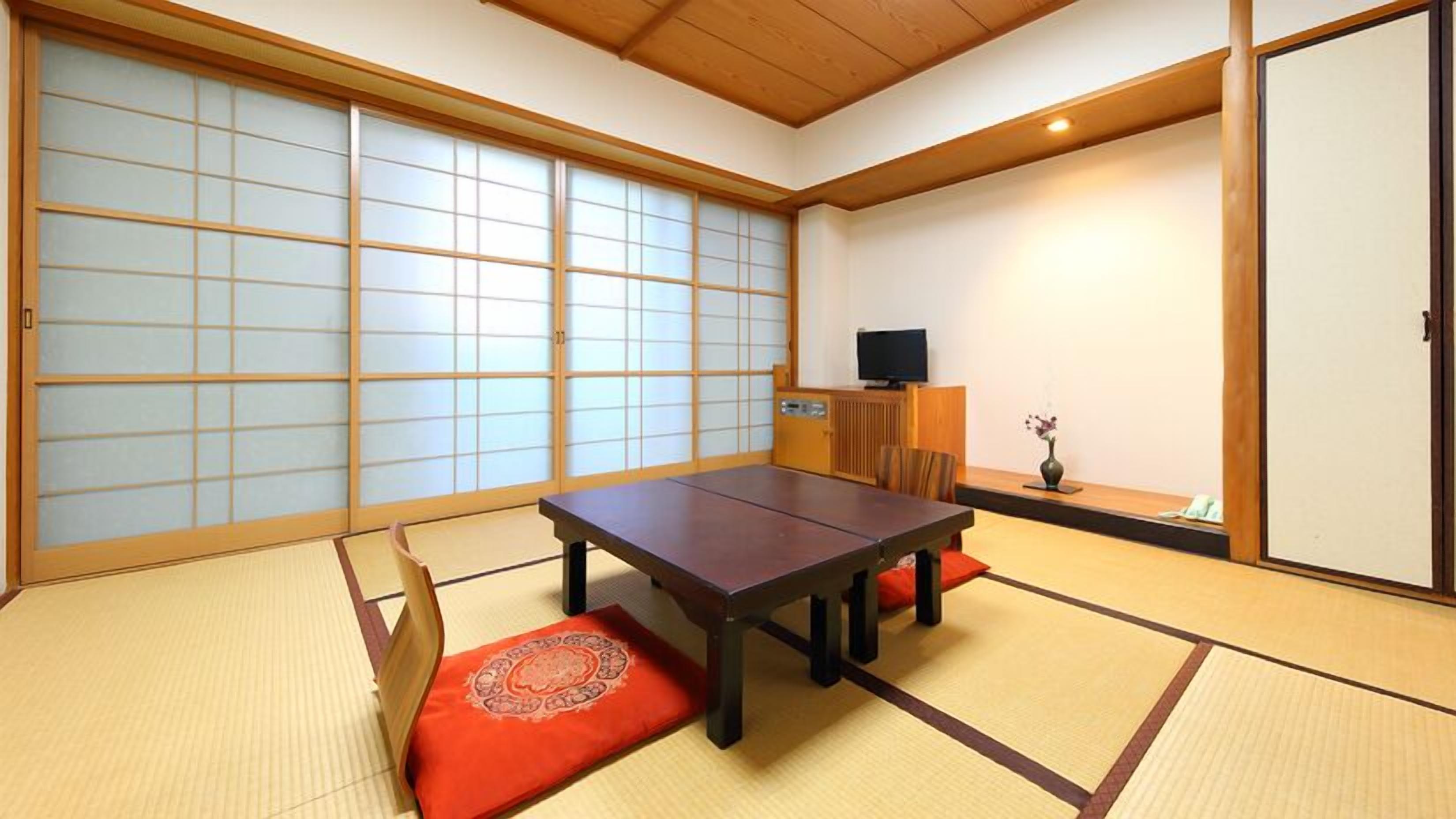 Ein traditioneller japanischer Raum mit Tatami-Böden, einem niedrigen Tisch mit Kissen, einem Fernseher und Schiebetüren.