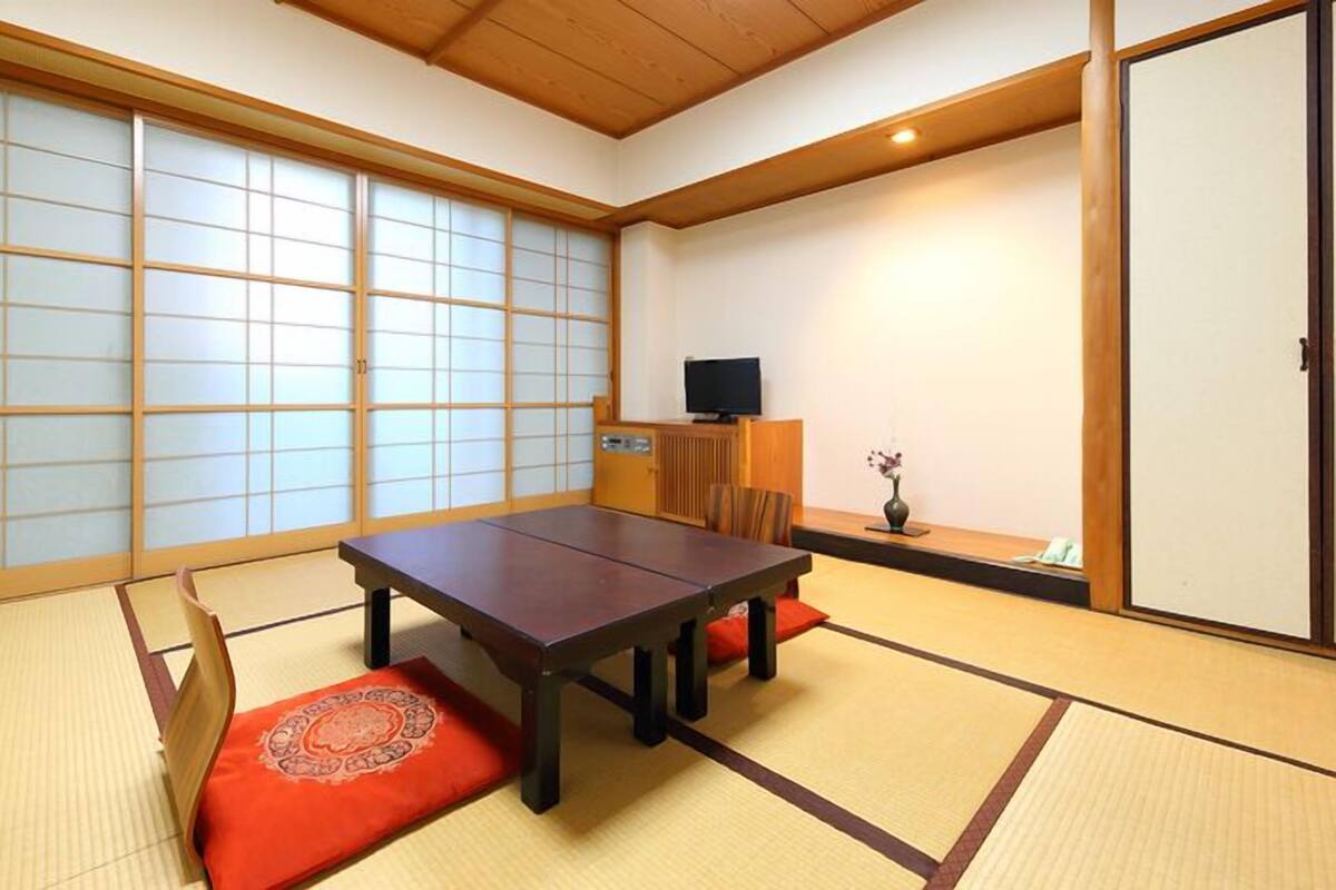 Een traditionele Japanse kamer met tatami vloerbedekking, een lage tafel met kussens, een televisie en schuifdeuren.