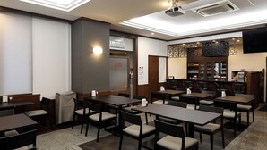 A restaurant with multiple tables and chairs, a bar area, and a projection screen on the wall. - Nagasaki IK Hotel (Nagasaki)