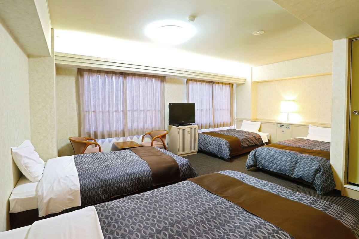 Een hotelkamer met drie bedden, een televisie, een bureau en een lamp.