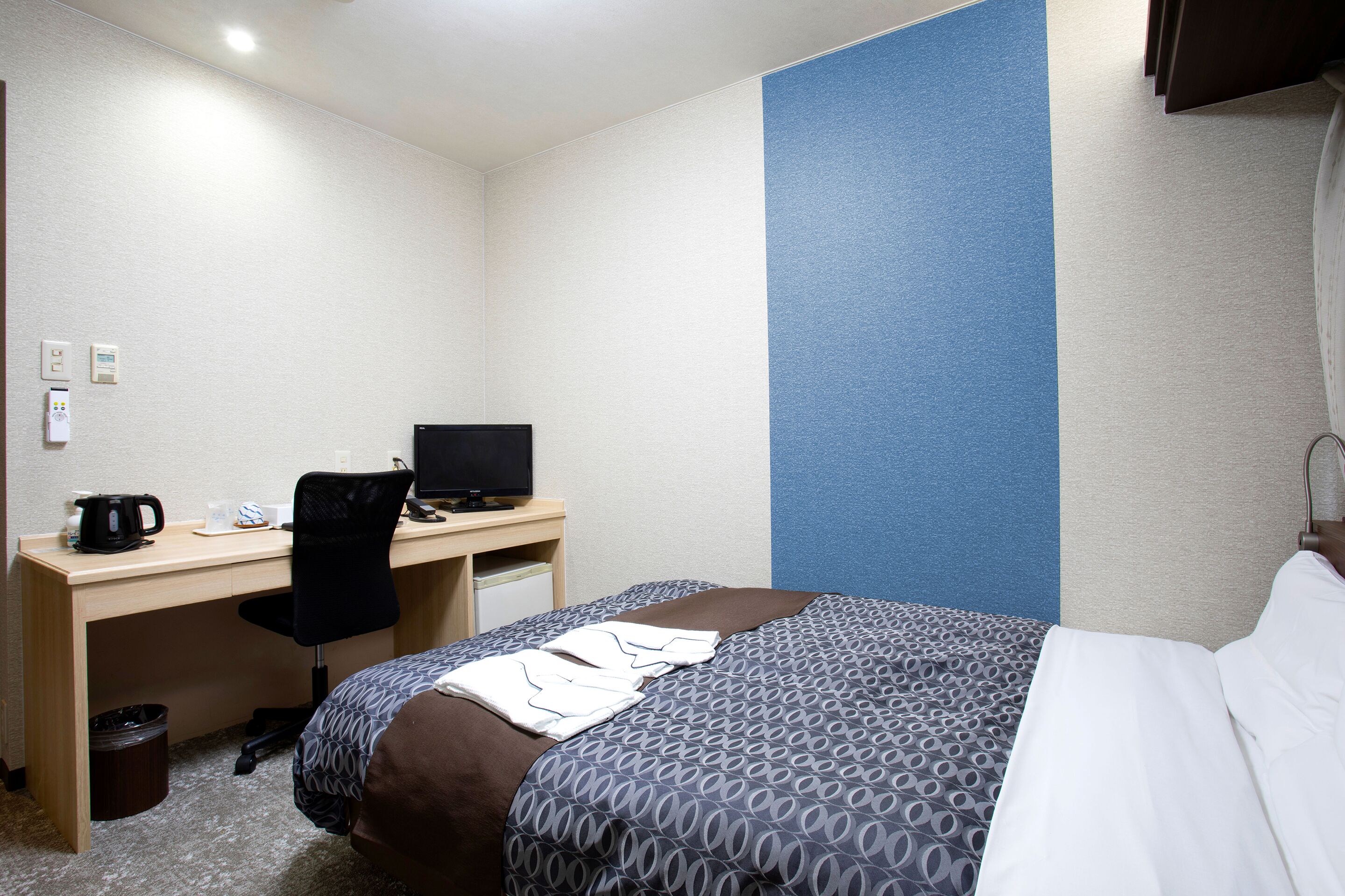 A hotel room with a bed, a desk with a computer, a chair, and a coffee maker.