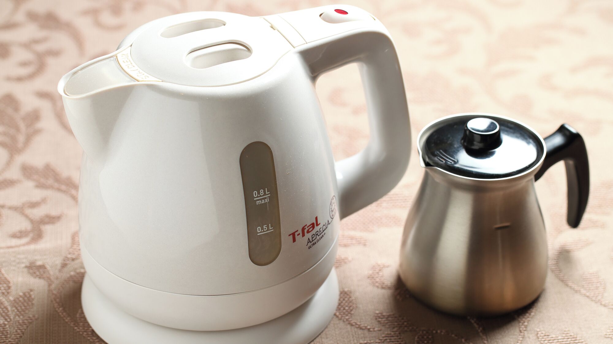 Ein weißes elektrisches Wasserkocher mit einem Griff und einer Edelstahl-Kaffeekanne.