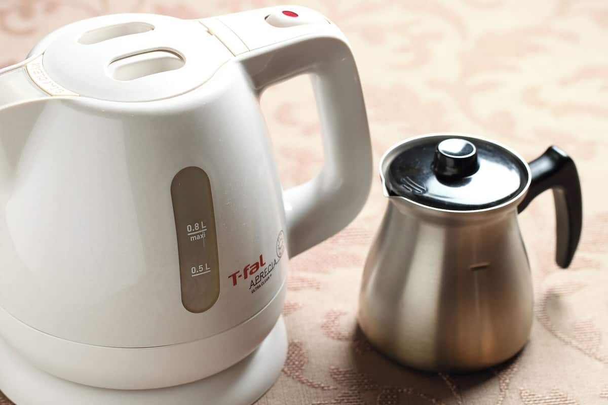A white electric kettle with a handle and a stainless steel coffee pot.