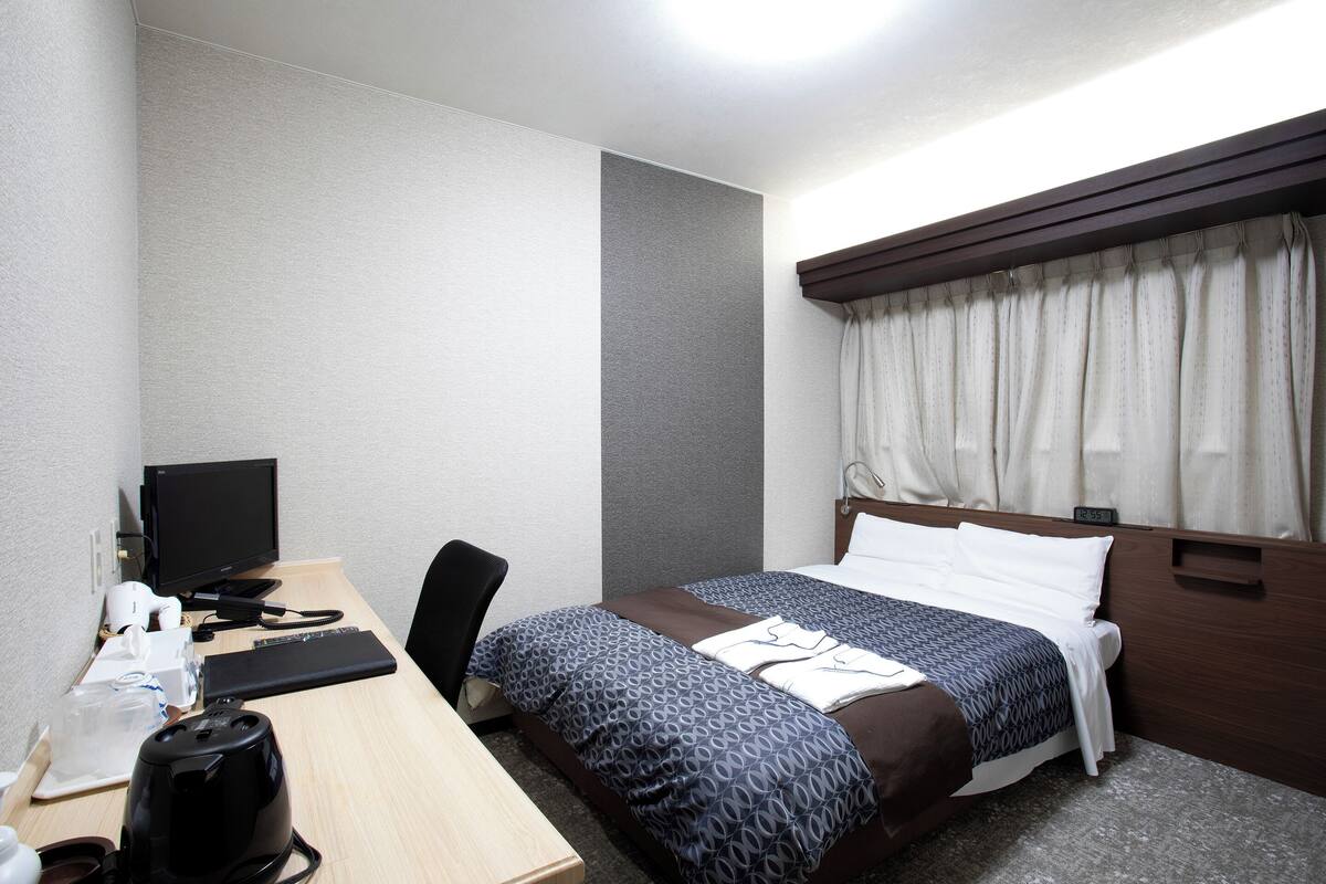 Een hotelkamer met een bed, een bureau met een computer, een stoel en een koffiezetapparaat.