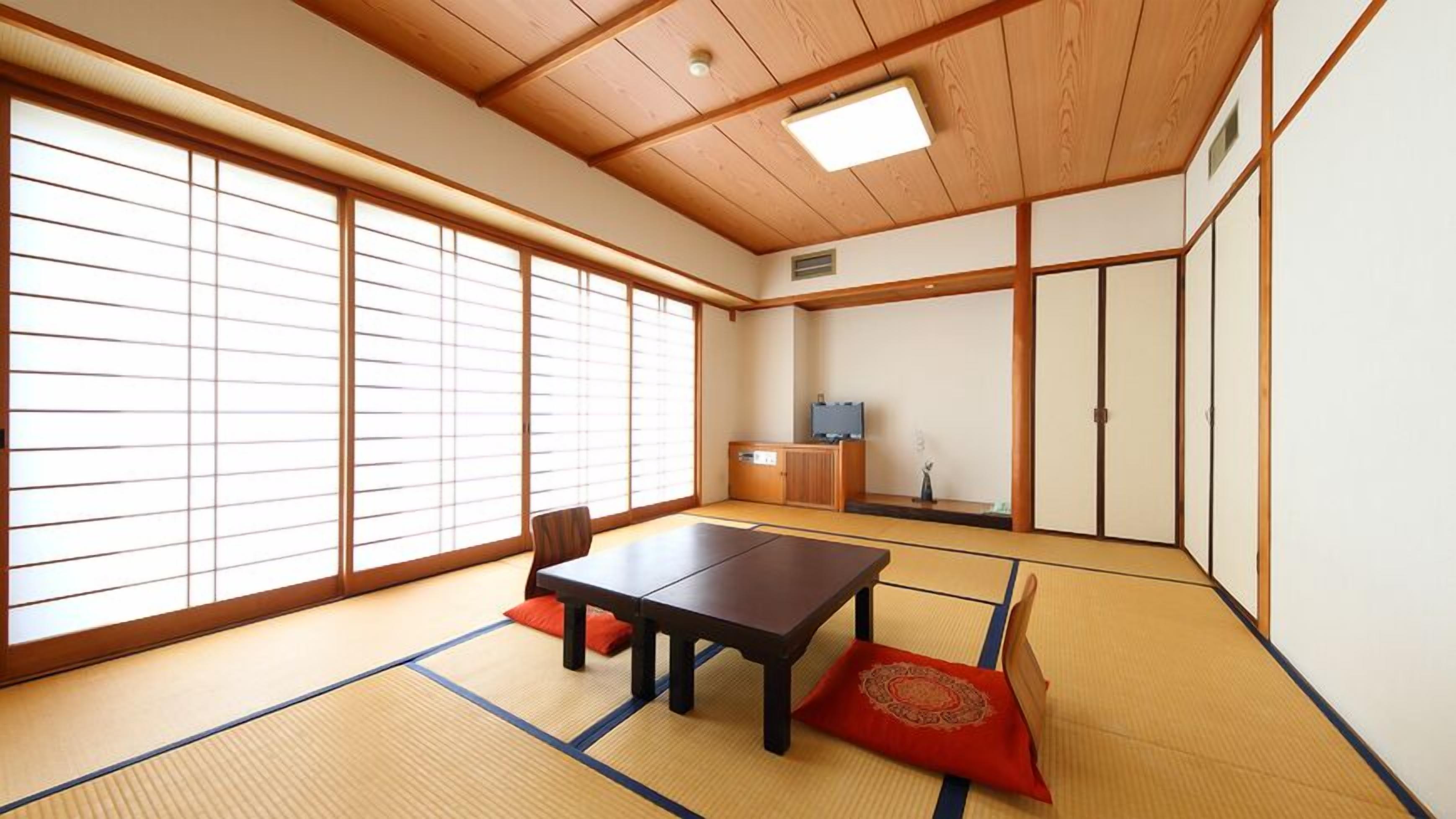 Ein traditioneller japanischer Raum mit Tatami-Boden, einem niedrigen Tisch, Schiebetüren und einem Fernseher.