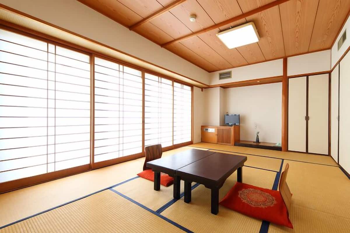 A traditional Japanese room with tatami flooring, a low table, sliding doors, and a television.