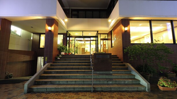 A hotel entrance with a set of stairs leading to the lobby, featuring a brick facade and potted plants. - Nagasaki IK Hotel (Nagasaki)