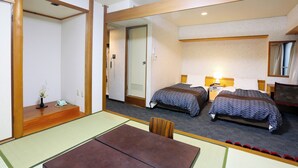 A hotel room with two beds, a sitting area with a table and chairs, and a small desk with a lamp. - Nagasaki IK Hotel (Nagasaki)