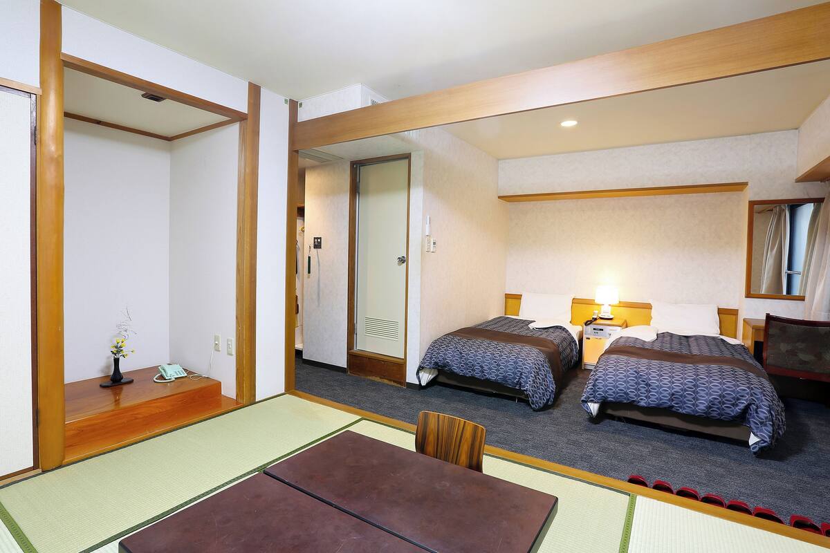 Een hotelkamer met twee bedden, een zithoek met een tafel en stoelen, en een klein bureau met een lamp.