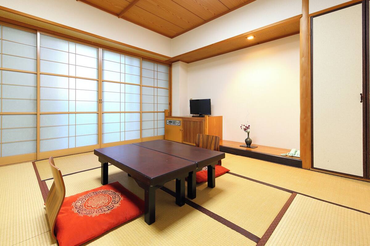 Een traditionele Japanse kamer met tatami vloerbedekking, een lage tafel met kussens, schuifdeuren en een televisie.