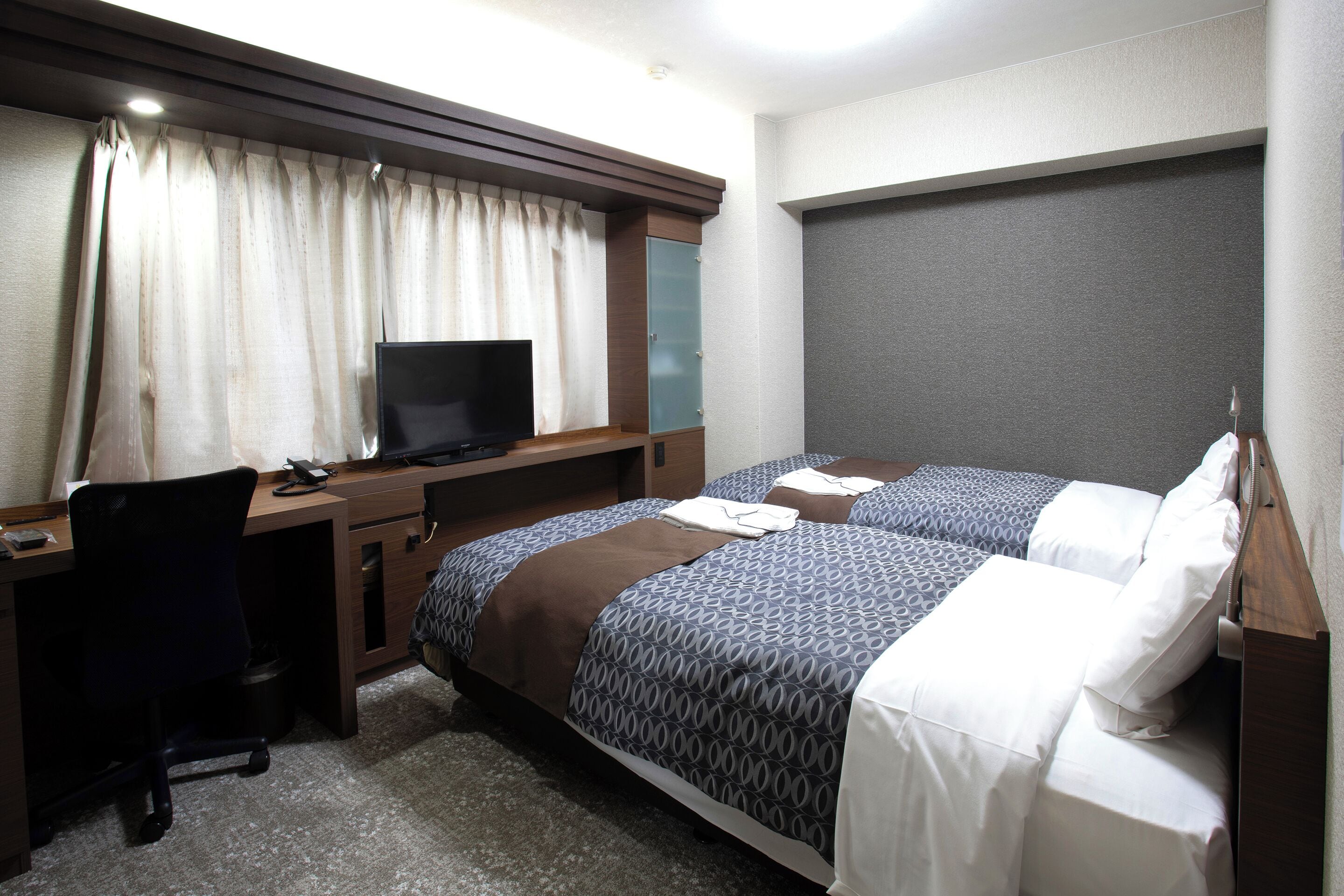 A hotel room with a desk, two beds, a television, and a large mirror.