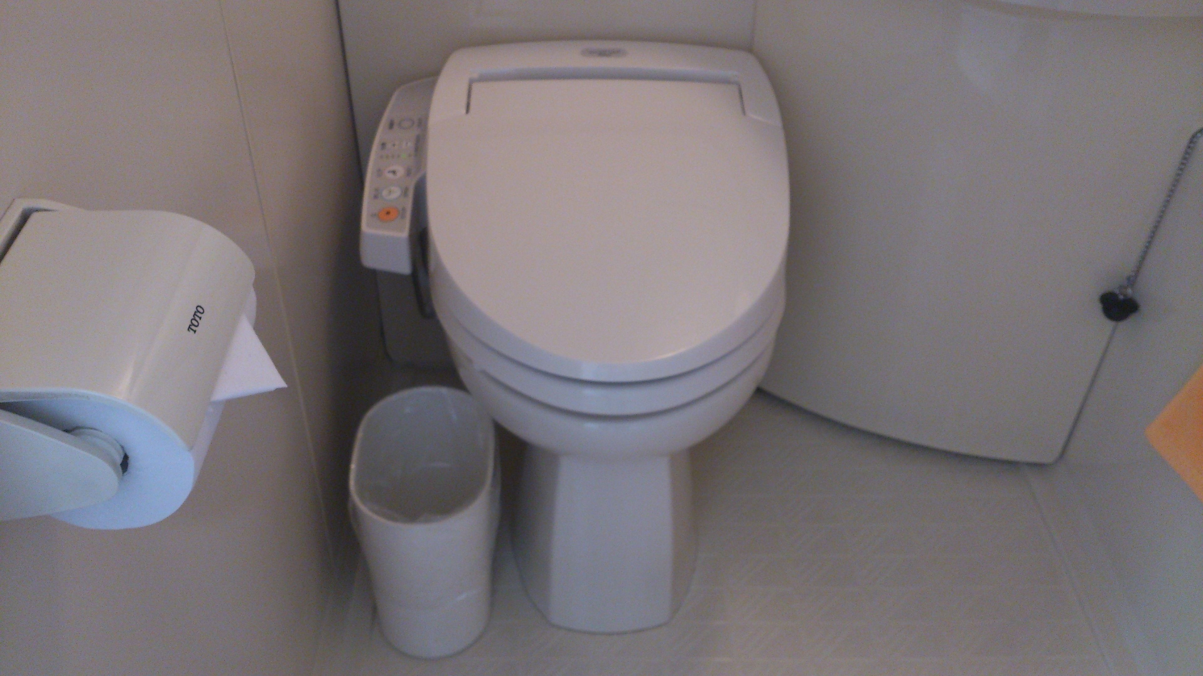 A toilet with a control panel, a toilet paper holder, and a trash bin.