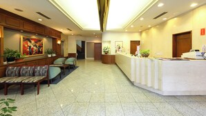 A hotel lobby with a reception desk, seating area, and artwork on the walls. - Nagasaki IK Hotel (Nagasaki)