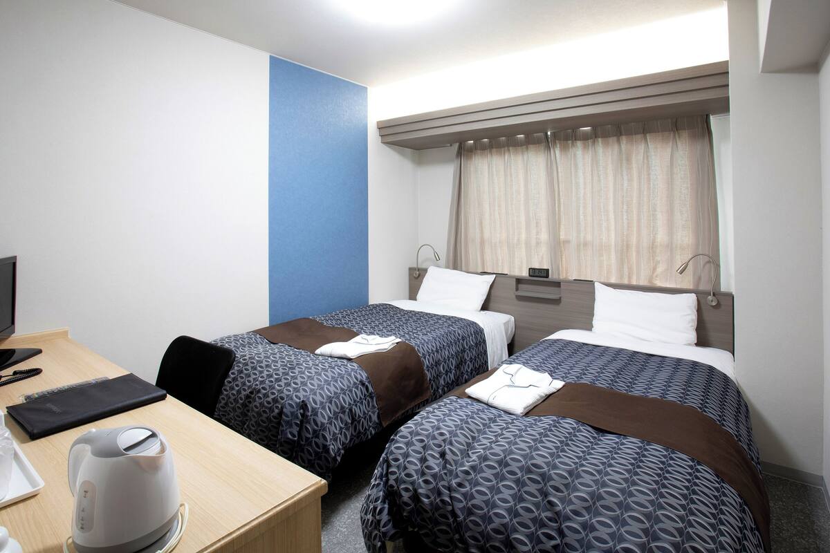 Een hotelkamer met twee bedden, een bureau, een waterkoker en een raam met gordijnen.
