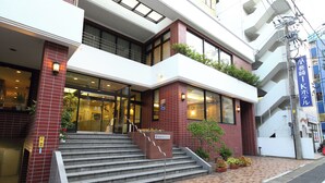 A hotel entrance with a set of stairs leading up to the entrance, a small garden area with potted plants, and a sign indicating the hotel's name. - Nagasaki IK Hotel (Nagasaki)