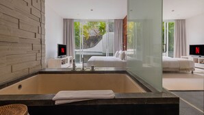 Een moderne badkamer met een groot bad, een douche met glazen wanden en uitzicht op een tropisch landschap.
