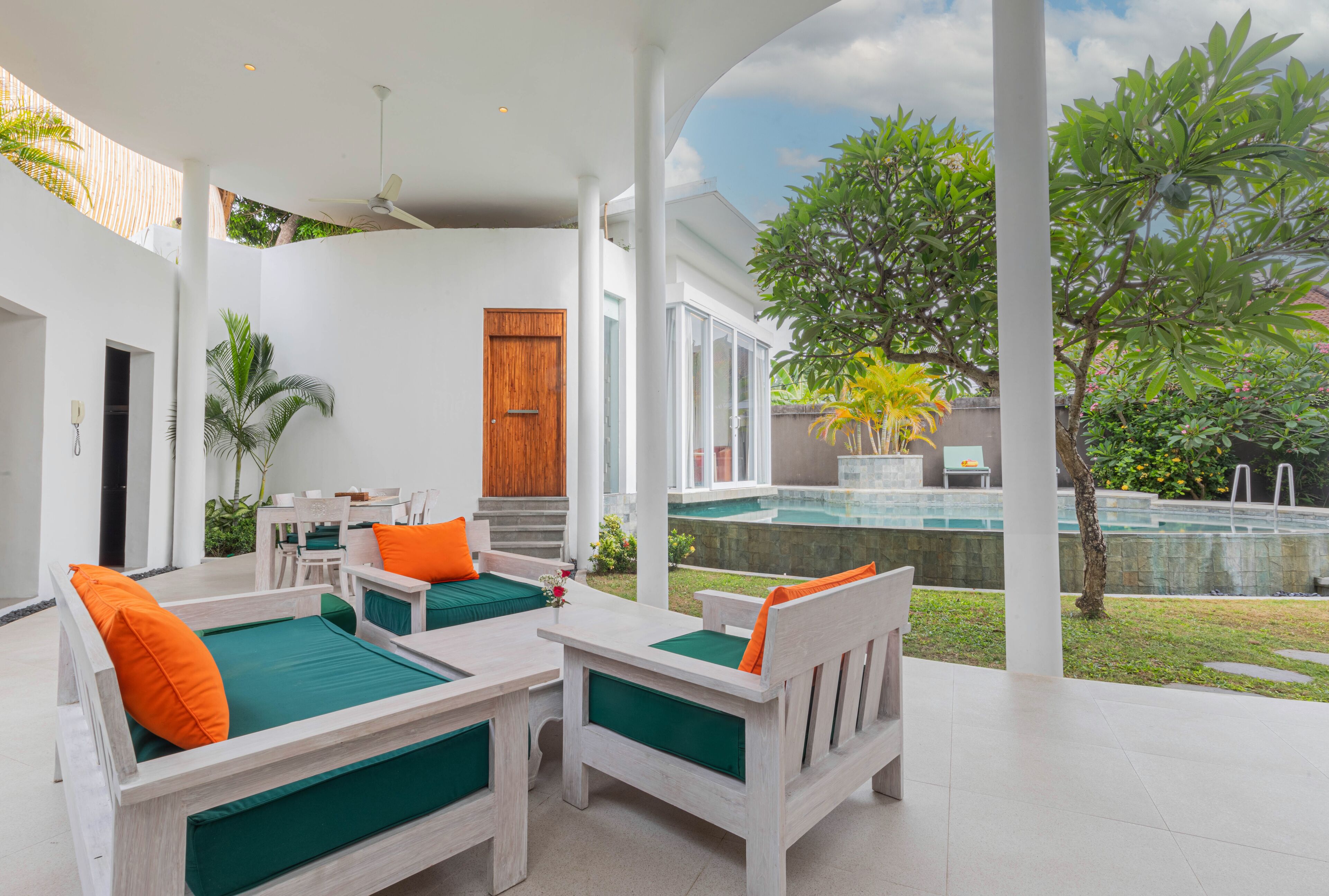 A modern outdoor seating area with white furniture and green cushions, overlooking a swimming pool and lush greenery.