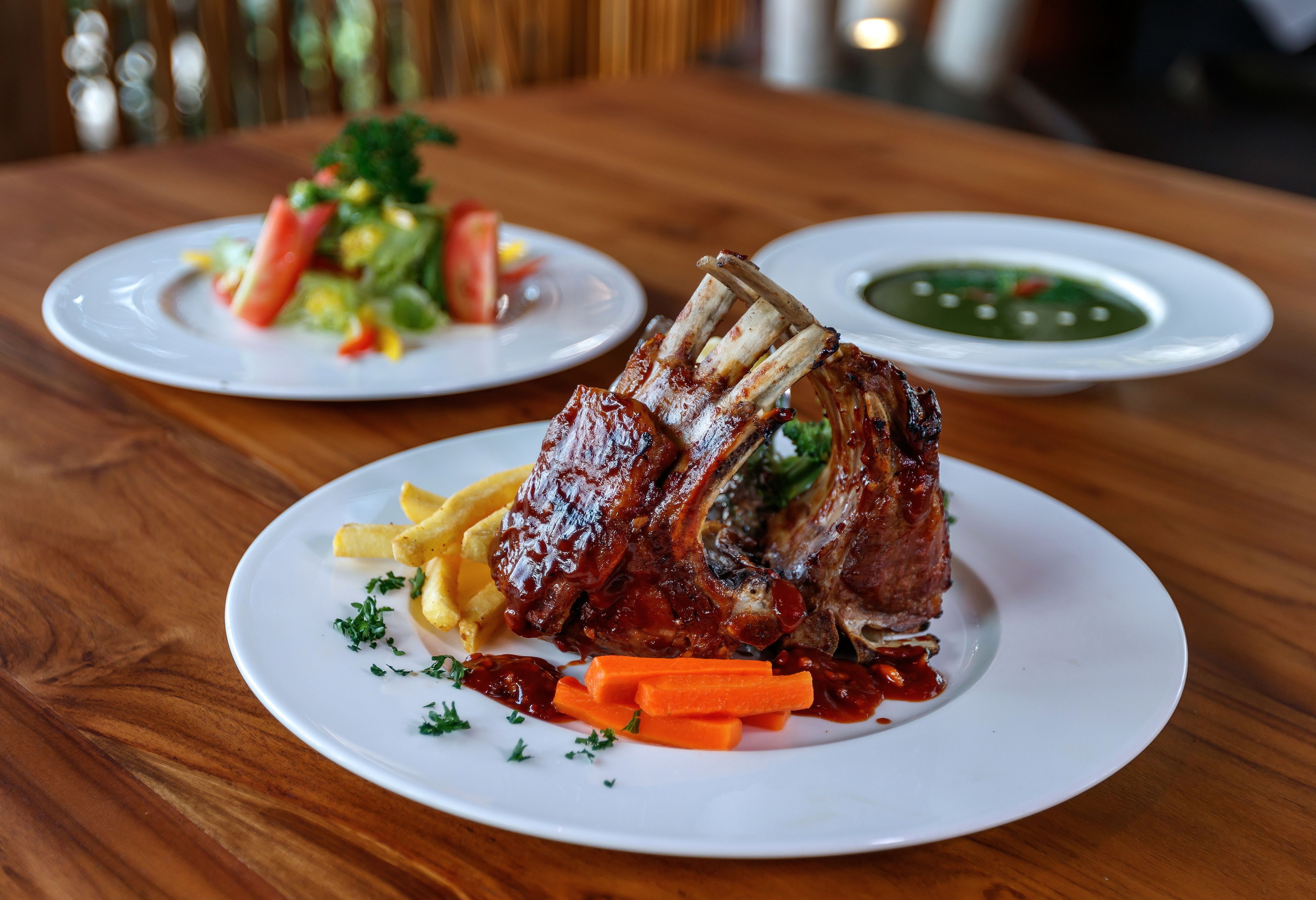 Una mesa de comedor con platos de comida, incluyendo costillas y vegetales.