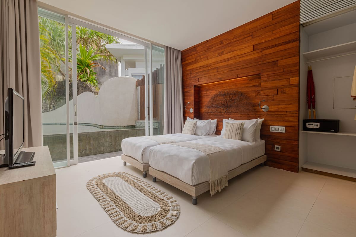 Quarto com uma cama grande, parede decorativa em madeira, porta de vidro deslizante para uma varanda e uma TV sobre uma escrivaninha.