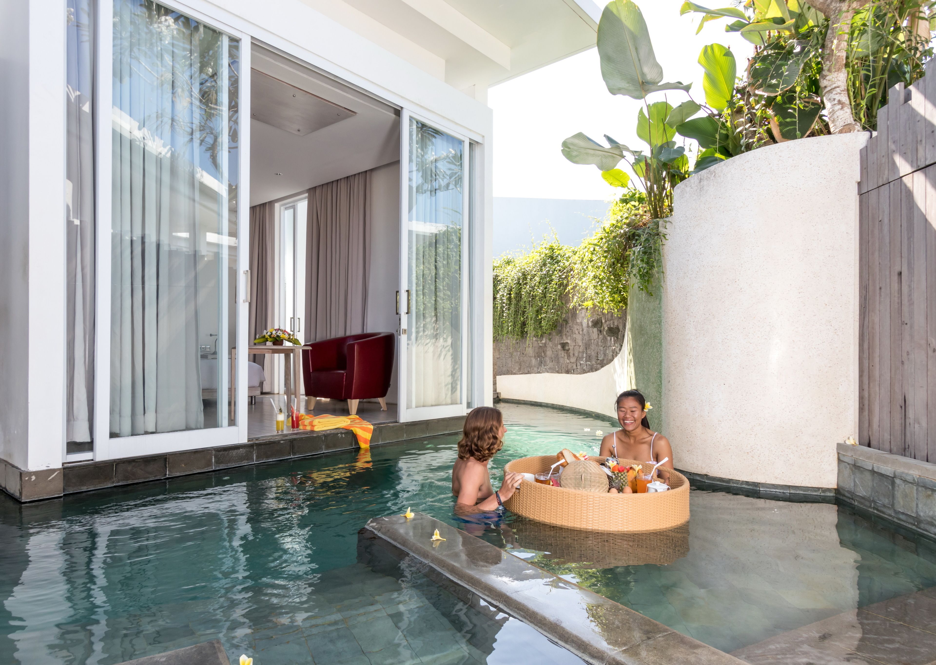 Un área de piscina con un espacio cubierto de vidrio, una silla roja y una bañera de mimbre.
