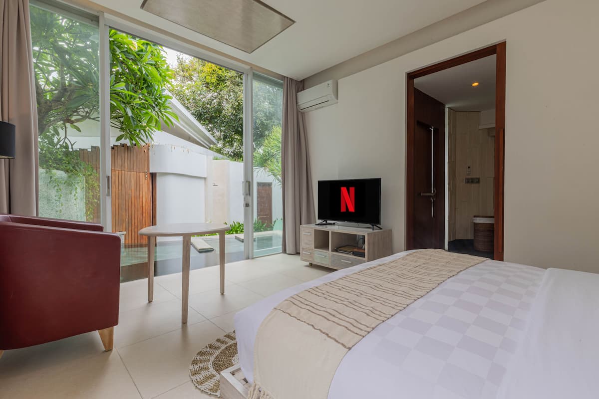 Quarto de hotel moderno com uma cama grande, televisão, mesa pequena e vista para o exterior.