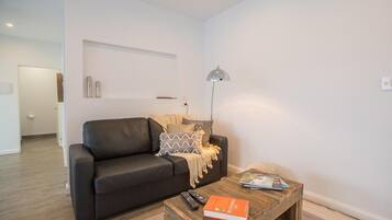 A modern living room with a dark leather sofa, a wooden coffee table with a book and remote control, and a floor lamp.