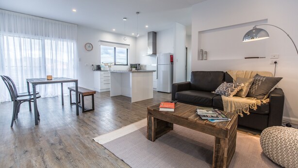 Un apartamento moderno con comedor, sala de estar con sofá, una mesa de centro y una cocina al fondo.