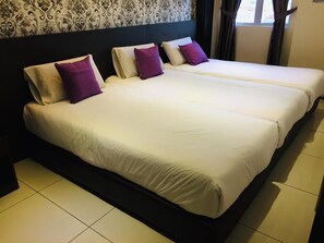 Una cama doble con sábanas blancas y almohadas moradas, un cabecero oscuro y un papel pintado con diseño.