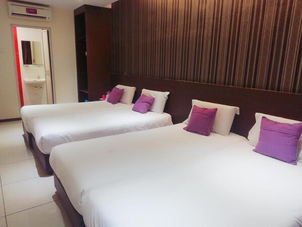 Habitación de hotel con dos camas, cada una con ropa blanca y almohadas moradas. Se aprecia un cabecero de madera y un espejo sobre las camas.