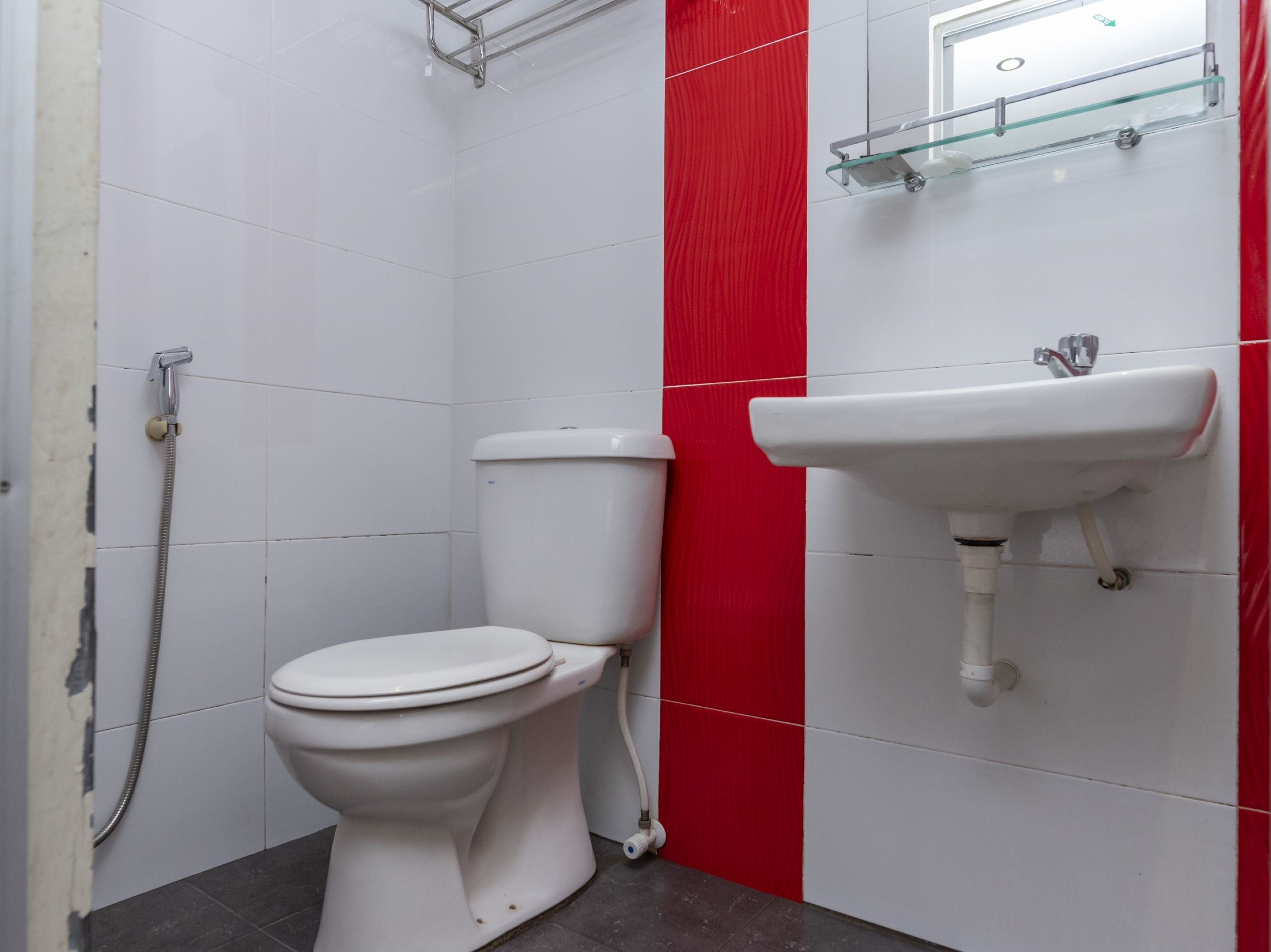 A bathroom with a white toilet, a red accent wall, and a glass shelf above a white sink.