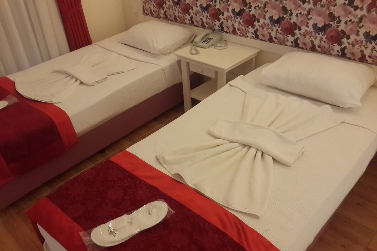 Two twin beds with red and white bedding, a small bedside table with a phone, and a floral-patterned wall.