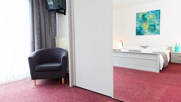 Hotelkamer met een rood tapijt, een zwarte fauteuil, een bed met wit bedlinnen, een nachtkastje, een lamp en een blauw abstract schilderij aan de muur.