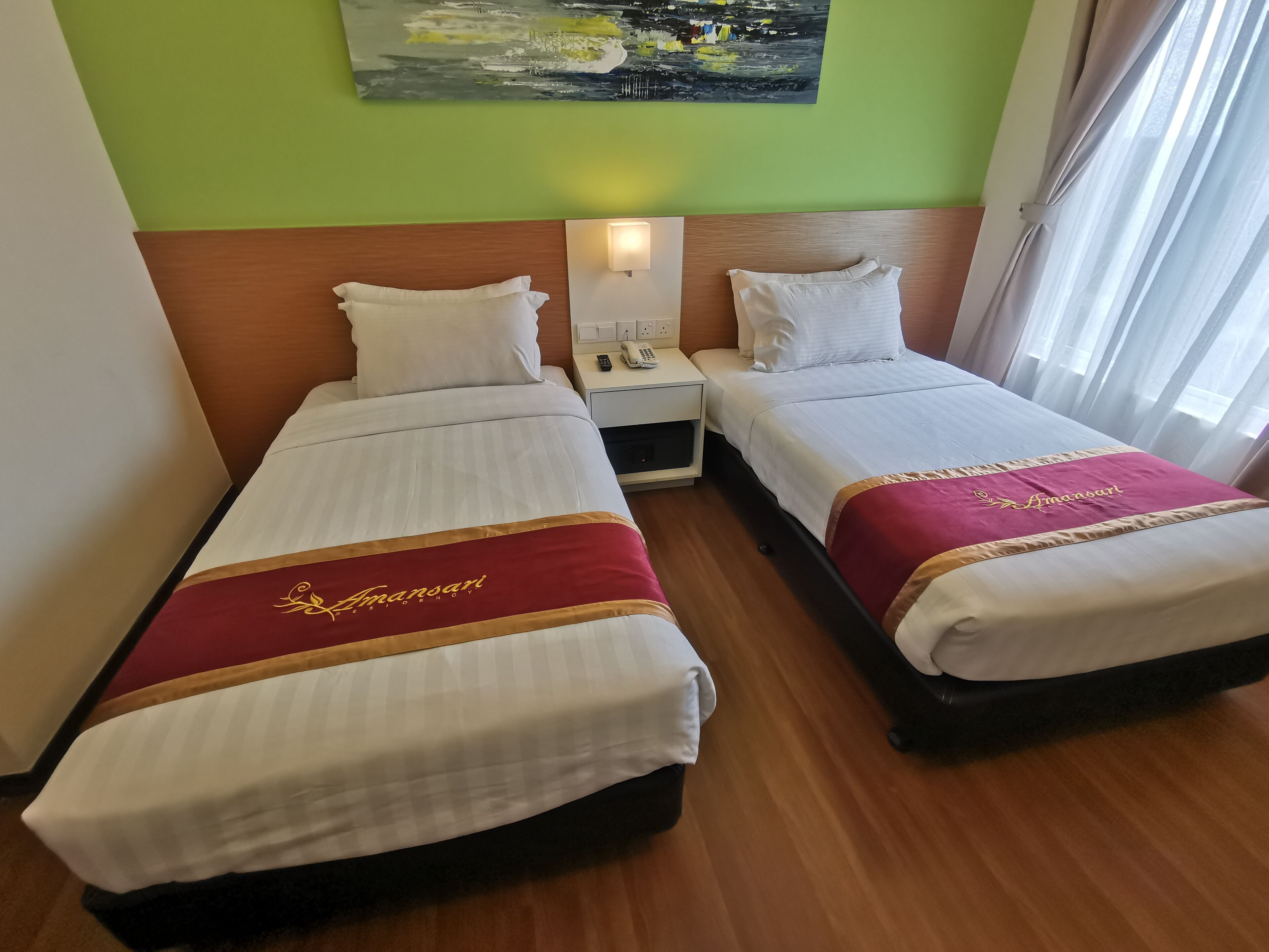 A hotel room with two single beds, each with a red and gold bedspread, white pillows, and a wooden headboard. There is a nightstand with a lamp and a phone between the beds.