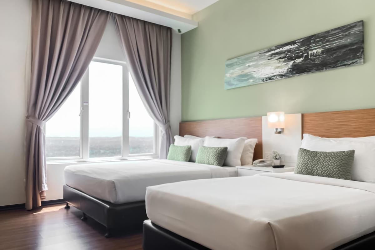 Ein Hotelzimmer mit zwei Betten, einem großen Fenster mit Vorhängen, einem Gemälde an der Wand und einem Nachttisch mit Lampe.