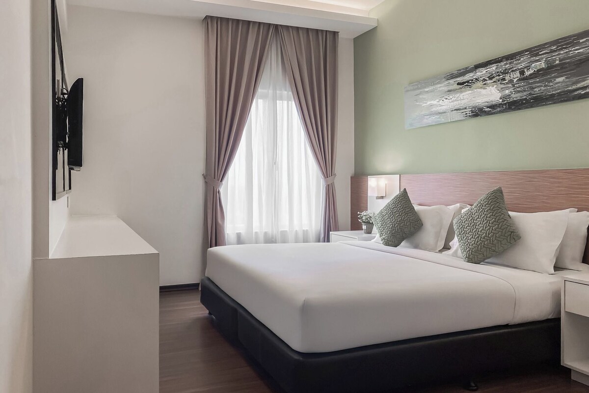 A hotel room with a large bed, a nightstand, a wall-mounted TV, and a window with curtains.