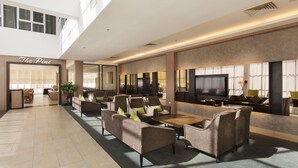 Un amplio vestíbulo con diseño moderno, que cuenta con una generosa zona de estar con sofás y sillones, un televisor de pantalla plana y un restaurante llamado "The Pine" al fondo.