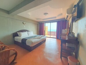 A hotel room with a bed, a desk, a chair, and a view of the sea through a sliding door. - Jirawan Hotel (Rayong)