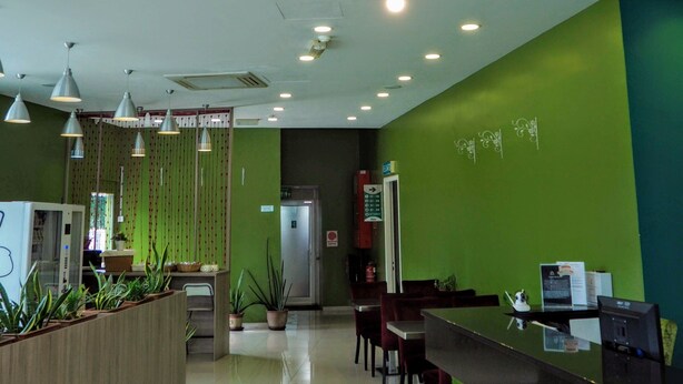 A reception area with a green wall, a modern chandelier, and a reception desk with computers. - Le Garden Hotel (Shah Alam)