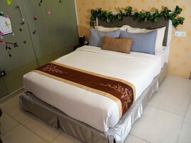 A neatly made bed with a decorative runner, a headboard with greenery, and a green wardrobe with a bird decal.