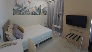 A hotel room with a bed, a desk with a telephone, a TV mounted on the wall, and a shower area with a curtain. - Le Garden Hotel (Shah Alam)