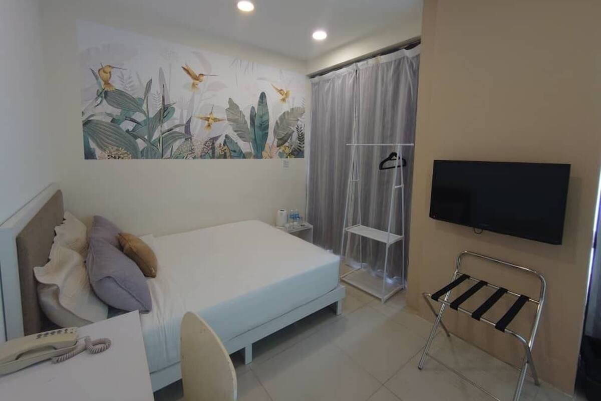 Ein Hotelzimmer mit Bett, Schreibtisch mit Telefon, Wandfernseher und Duschbereich mit Vorhang.