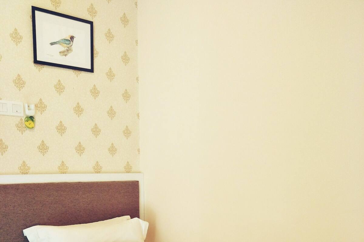 Ein ordentlich bezogenes Bett mit weißer und brauner Bettwäsche, ein Kopfteil und ein gerahmtes Bild von einem Vogel an der Wand.