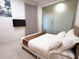 A hotel room with a bed, a television mounted on the wall, a wardrobe, and a window with curtains.