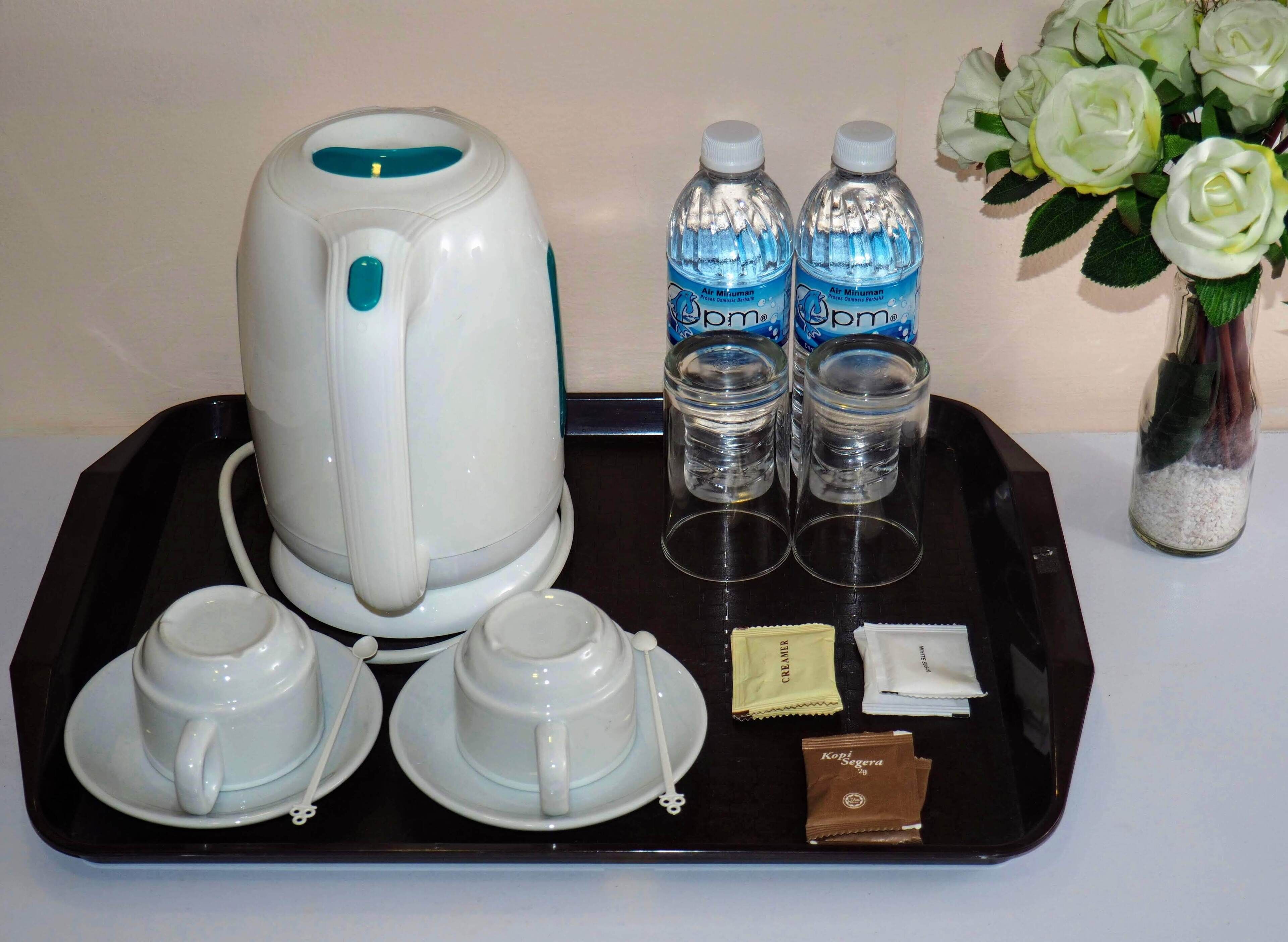 A tea set with a kettle, two cups, and a tray with two bottles of water, a creamer packet, and a coffee creamer packet.