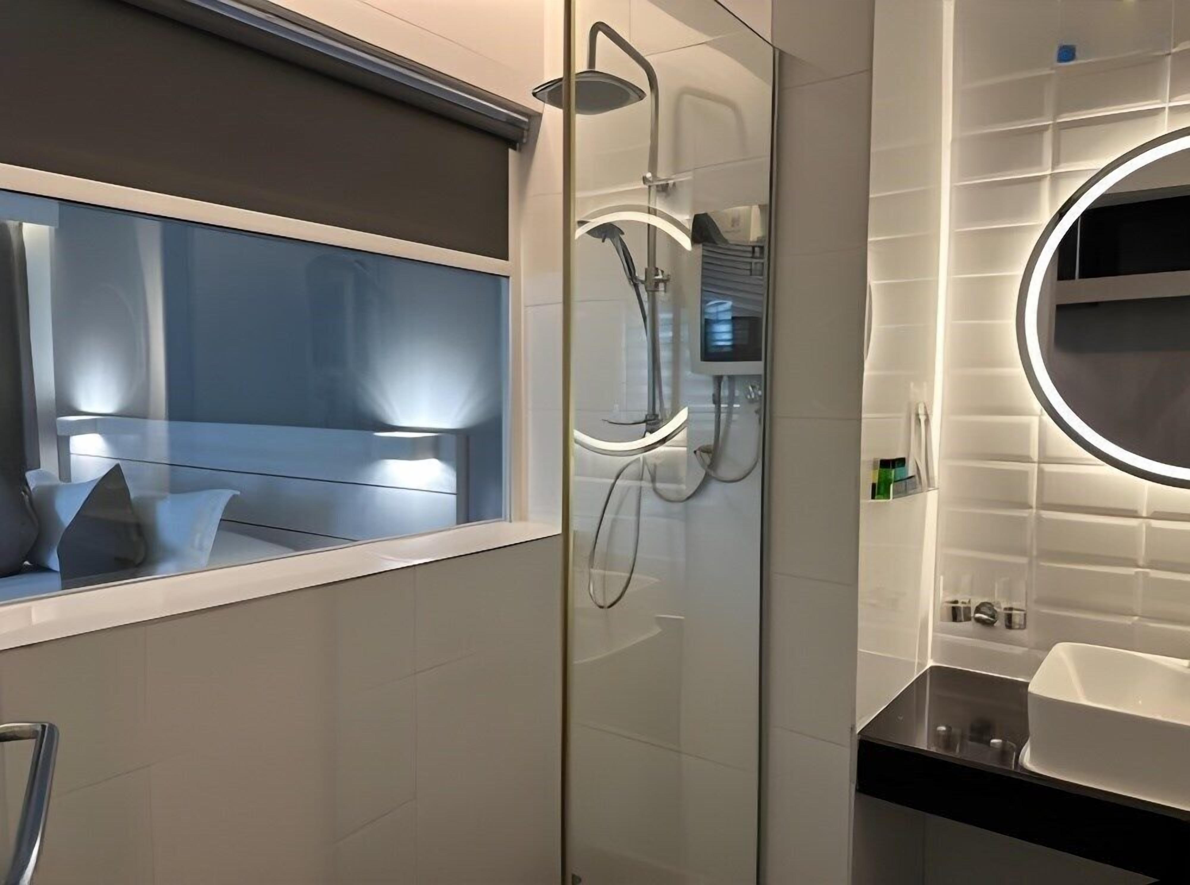 Een moderne badkamer met een douchecabine van glas, een wastafel met spiegel en een raam met uitzicht.