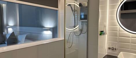 Un baño moderno con cabina de ducha de vidrio, tocador con espejo y ventana con vistas.