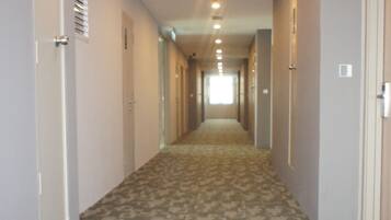 A hotel hallway with carpeted floors, doors on both sides, and a ceiling with recessed lighting.
